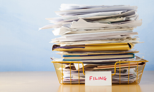 Stack of papers in filing bin on desk.