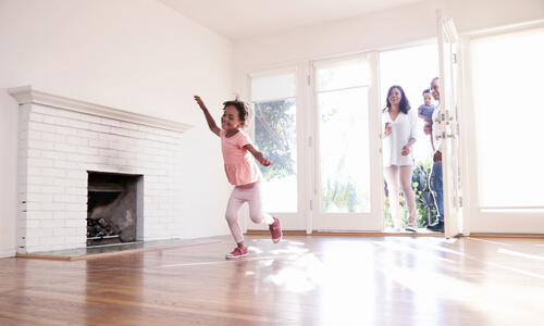 Husband and wife walking into a new home, their child dancing in living room. Made possible by a credit union mortgage.