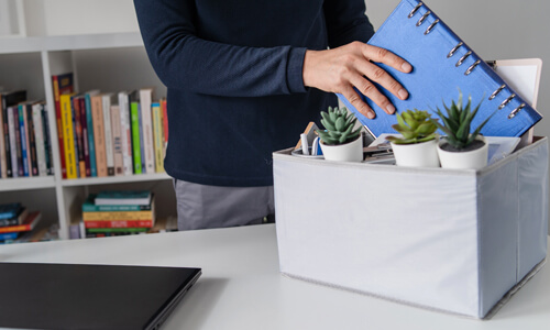 Man cleaning out his desk after a layoff and taking out a notebook to work on his finances.